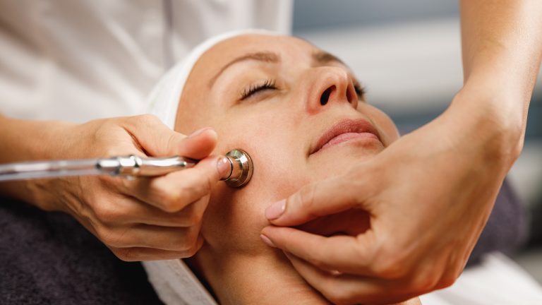 Gesichtsreinigung, Technologien für deine Skin Care Eine Person liegt auf einer Liege in einem Salon und bekommt die Haut auf ihrer Wange gereinigt.