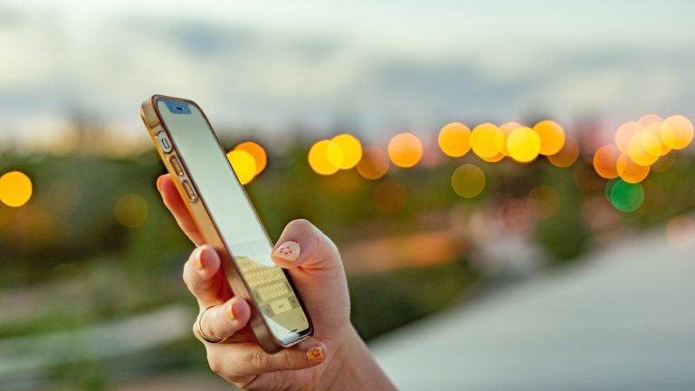 KI vs Smart, Warum das nicht immer gleich ist Eine Person hält ein Handy in der Hand und tippt darauf. Im Hintergrund sind viele Lichtpunkte.