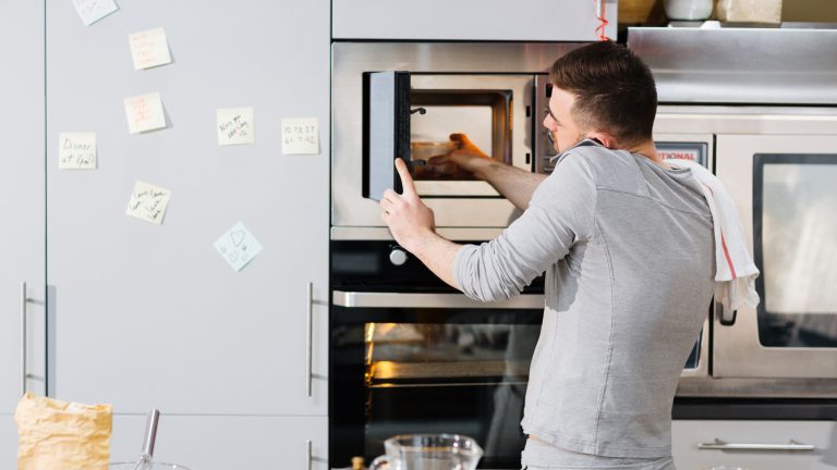Mikrowellenfunktionen, Erklärungen und Tipps zur Nutzung Eine Person stellt eine Schüssel mit Essen in die Mikrowelle während sie nebenbei telefoniert.