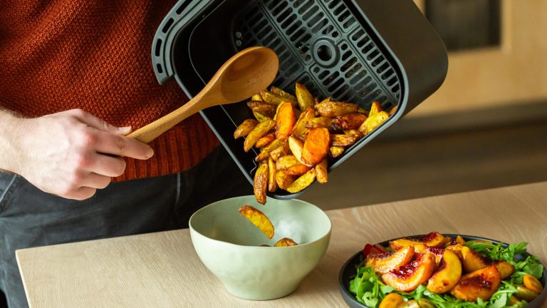 Philips 3000 Series Dual Basket Airfryer, Doppelt gut Eine Person gießt einige Kartoffelspalten von einem Airfryer-Korb in eine Schüssel.