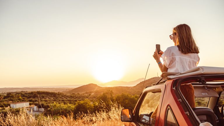 Smartphones unter 300 Euro, 5 günstige Handys Eine Person steht in einem Auto und fotografiert eine Landschaft und den Sonnenuntergang durch das offene Verdeck.