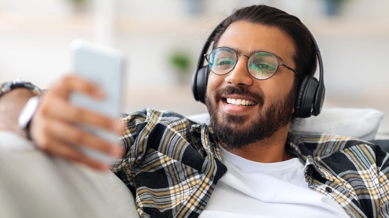 Twitch-Abo, Einfach und schnell kündigen Eine Person sitzt mit Kopfhörern auf einer Couch und schaut auf ihr Smartphone.