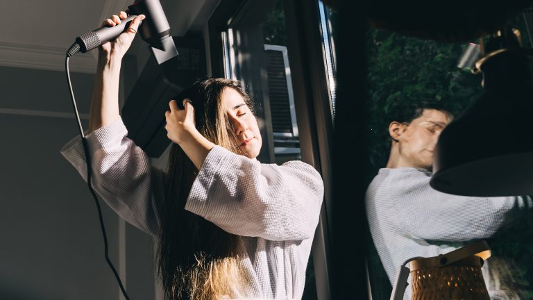 Ionen-Haartrockner, Was steckt hinter der Technik Eine Person steht im Raum und trocknet ihre Haare.