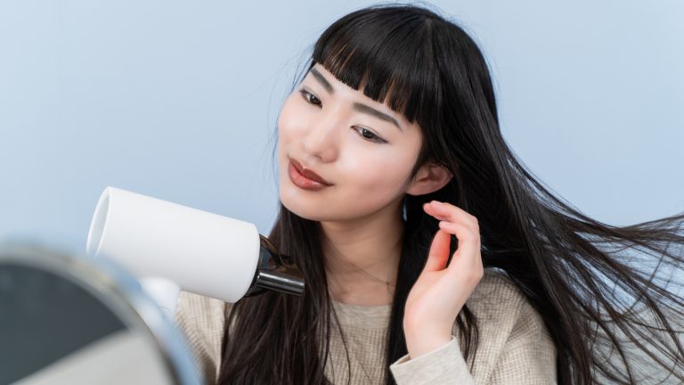 Ionen-Haartrockner, Was steckt hinter der Technik Eine Person sitzt vor einem Spiegel und föhnt sich die Haare.