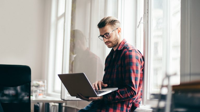 Passkey, Was sie sind und wie sie funktionieren Eine Person lehnt an einem Fenster und hält einen Laptop in der Hand.