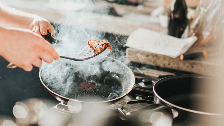 Rauchmelder piept, Mögliche Gründe und Lösungen In einer dampfenden Pfanne wird ein Stück Bacon gebraten.