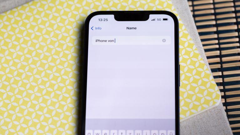 Ein iPhone liegt auf einer gelb-wei&szlig;en Oberfl&auml;che. Auf dem Display ist die Namens&auml;nderung des Ger&auml;ts zu sehen