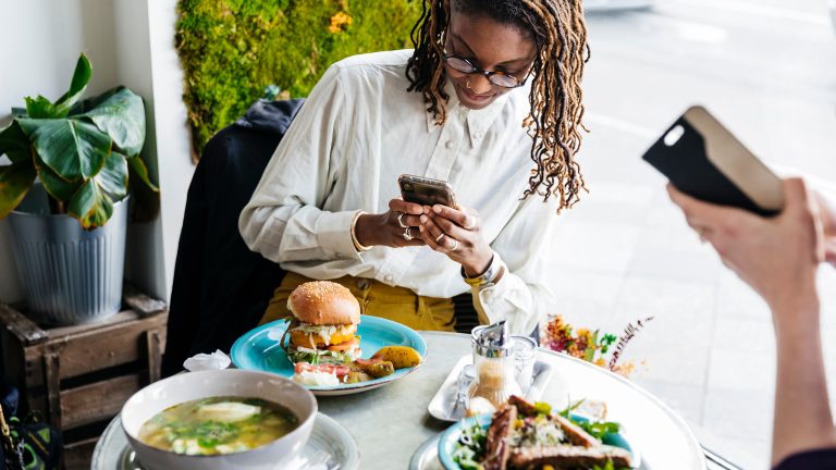 Food Fotografie, Tipps und Tricks um leckeres Essen gut zu inszenieren Eine Person schießt mit ihrem Smartphone ein Foto von einem Burger im Restaurant.