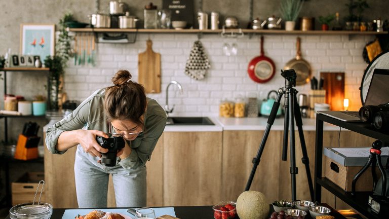 Food Fotografie, Tipps und Tricks um leckeres Essen gut zu inszenieren Eine Person steht in einer Studioküche und macht professionelle Aufnahmen von Essen mit einer Digitalkamera.