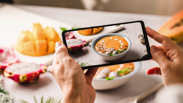 Food Fotografie, Tipps und Tricks um leckeres Essen gut zu inszenieren Nahaufnahme der Hände einer Person, die mit dem Smartphone ein Foto einer herbstlichen Bowl schießt.