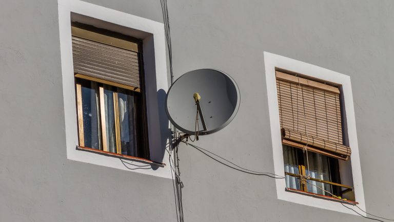 Satellitenschuessel montieren und ausrichten, So machst du es richtig Eine Satellitenschüssel ist an einer Wandhalterung an einer Hauswand befestigt.