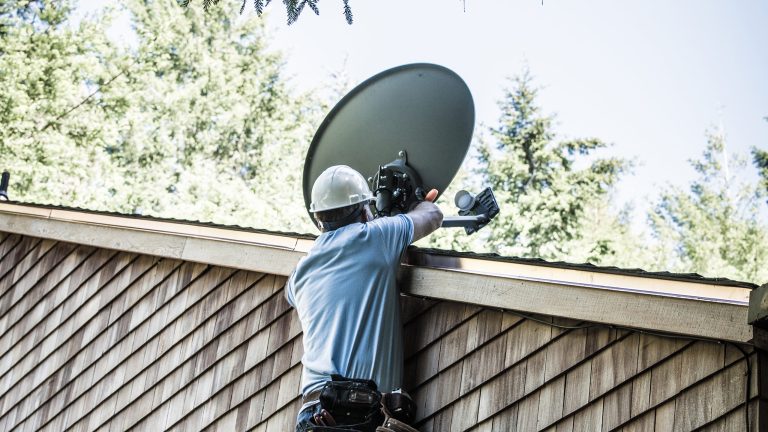 Satellitenschuessel montieren und ausrichten, So machst du es richtig Eine Person mit Helm richtet eine Satellitenschüssel auf einem Dach aus.