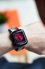 Eine Person trägt eine Smartwatch am linken Handgelenk und checkt die Herzfrequenz auf dieser.
