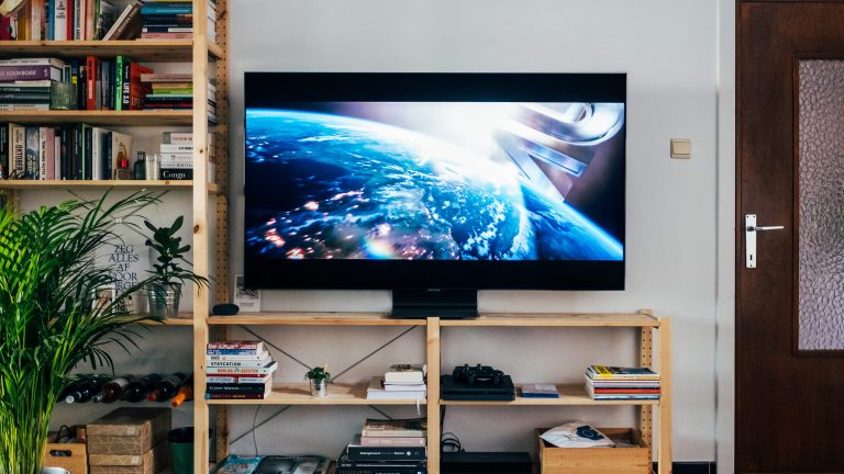 Full-HD, 4K und Co., HD-Auflösungen im Überblick Ein Fernseher steht auf einem Holz-Lowboard in einem Wohnzimmer. Es beginnt gerade ein Spielfilm.