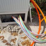 Ein Verteilerkasten ist unten geöffnet. Heraus kommen zahlreiche Glasfaserkabel.