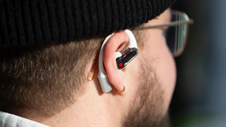 Nothing Ear (open), Stilvolles Design und innovative Technologie Eine Person mit Brille trägt einen Nothing Ear (open) Bud im Ohr. Der Ohrbügel schmiegt sich um das Ohr und darunter lugt der Brillenbügel der Person hervor.