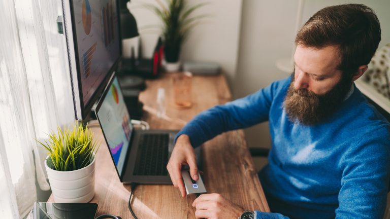 USB-Stick wird nicht erkannt, Gründe und Lösungen Eine Person sitzt am Tisch vor einem Laptop und versucht mithilfe eines USB-Anschlusses eine externe Festplatte zu verbinden.