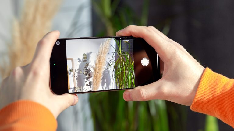 Eine Person h&auml;lt ein iPhone 16 in zwei H&auml;nden und macht damit ein Foto im Querformat.