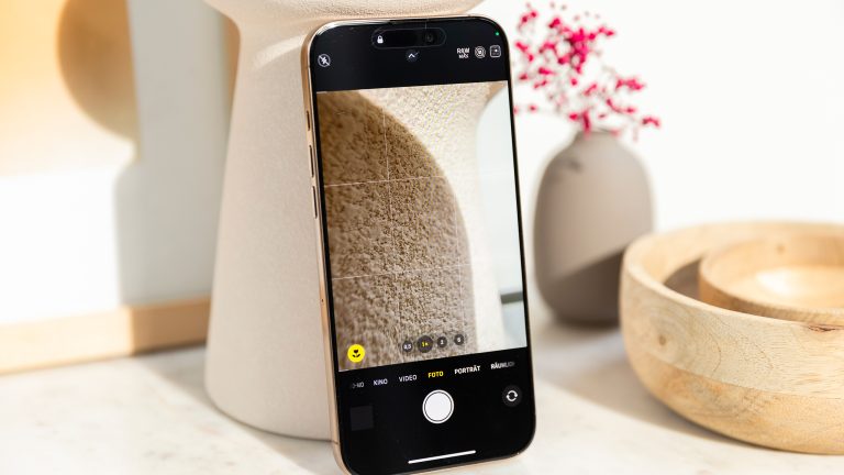 Fotos bearbeiten auf dem iPhone Ein iPhone mit geöffneter Kamera-App lehnt an einer beigen Vase. Ein Foto im RAW-Format zeigt die Details der Struktur der Vase.
