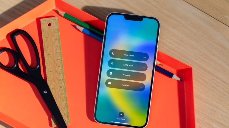 So bringst du mehr Achtsamkeit in dein Leben Ein iPhone 14 Plus liegt in einer orangefarbenen Schale auf einem Holztisch. Der „Fokus“-Modus ist geöffnet.