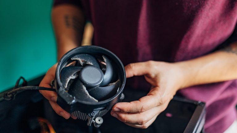 Frühjahrs-Check für deine PC-Hardware, So machst du sie fit Eine Person hält einen CPU-Lüfter in der Hand, dessen Lüfterflügel deutlich sichtbar verstaubt sind.