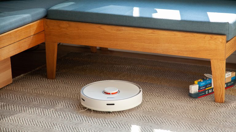 Ein Roborock S5 Max fährt über einen Teppich vor einer Sitzbank.