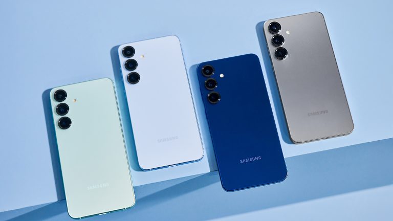 Vier Samsung Galaxy-S25-Handys liegen auf einer blauen Oberfläche nebeneinander.