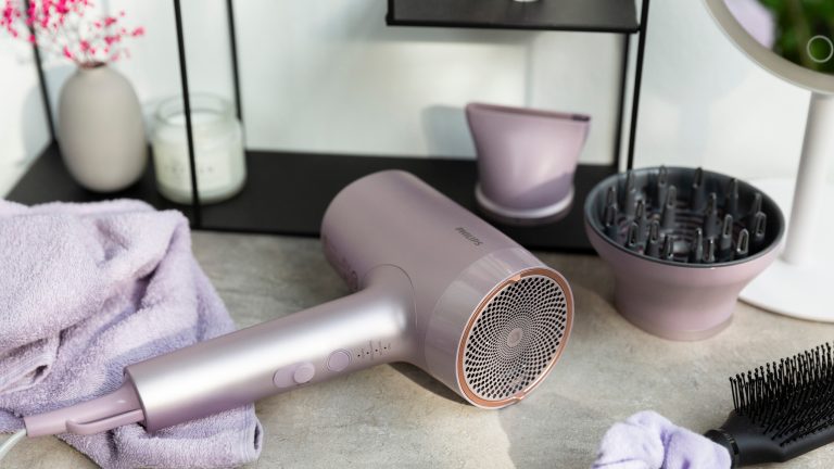Glanz, Schutz, Power, der Philips 7000er Haartrockner im Praxistest Der Haartrockner Philips 7000er liegt auf einem Tisch im Badezimmer umgeben von verschiedenem Zubehör, wie seinen Aufsätzen, einer Bürste und einem Haargummi.