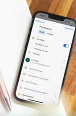 Ein iPhone liegt auf einem Notizblock. Auf dem Display ist ein erstellter Eintrag im Google Kalender für einen Urlaub zu sehen.