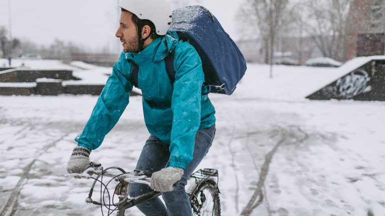 Eine Person mit einem Rucksack auf dem Rücken ist bei Schnee mit einem Fahrrad unterwegs.