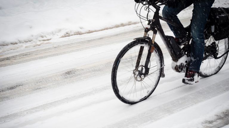 E-Bike im Winter fahren, Das solltest du beachten Auf einer schneebedeckten Straße fährt eine Person mit einem E-Bike.