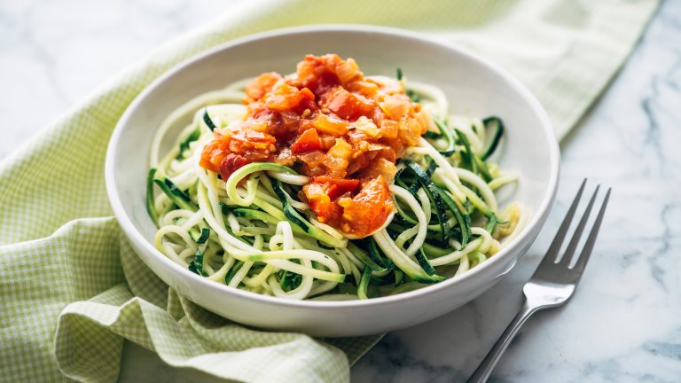 Gesund ernähren leicht gemacht, Mit diesen Geräten klappt’s Auf einem Teller befinden sich Zucchini-Nudeln, die teilweise von etwas Tomatensauce bedeckt werden.