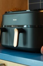 Eine schwarze Philips 3000 Series Heißluftfritteuse steht auf einem Küchenregal. Daneben liegen Aprikosen, Karotten und Kartoffeln.