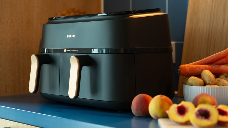 Eine schwarze Philips 3000 Series Heißluftfritteuse steht auf einem Küchenregal. Daneben liegen Aprikosen, Karotten und Kartoffeln.