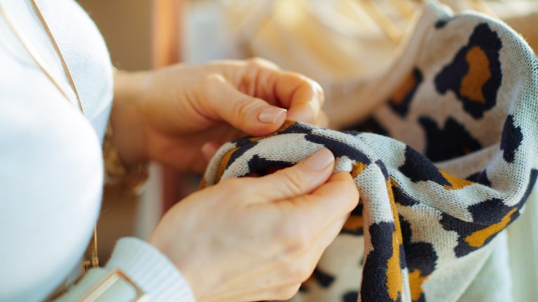 Kleidermotten bekämpfen, so erkennst und beseitigst du die Schädlinge Eine Person hält ein Kleidungsstück in beiden Händen und inspiziert den Stoff.