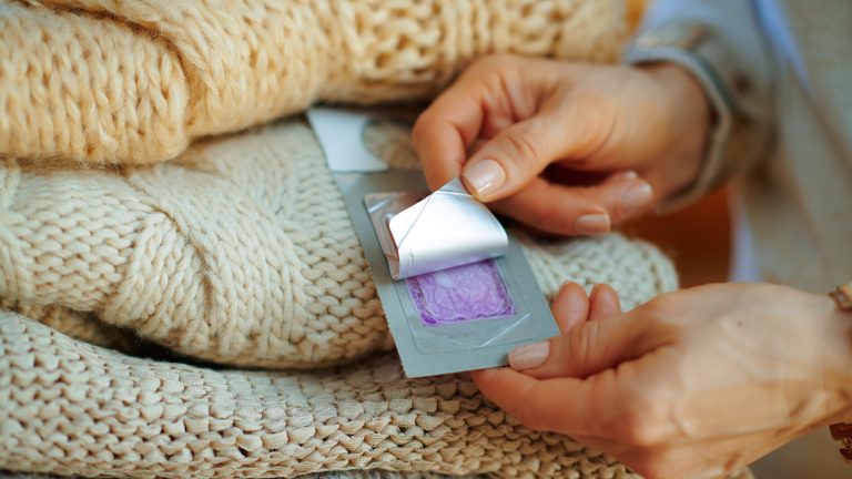 Kleidermotten bekämpfen, so erkennst und beseitigst du die Schädlinge Eine Person zieht die Lasche einer Klebefalle für Kleidermotten ab. Daneben liegt ein Stapel von Textilien aus Wolle.
