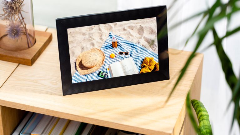 Minimalistisch leben, Mit digitalen Tools und analogen Hilfsmitteln entrümpeln-leben-1 Ein digitaler Bilderrahmen steht auf einem Bücherregal. Er zeigt das Foto einer Strandszene.