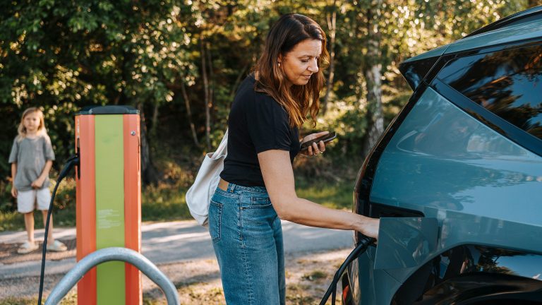 Эко-товар leben, So machst du deinen Alltag grüner Eine Person steht an einer Ladesäule und steckt einen Stecker in ein E-Auto, um es zu laden.