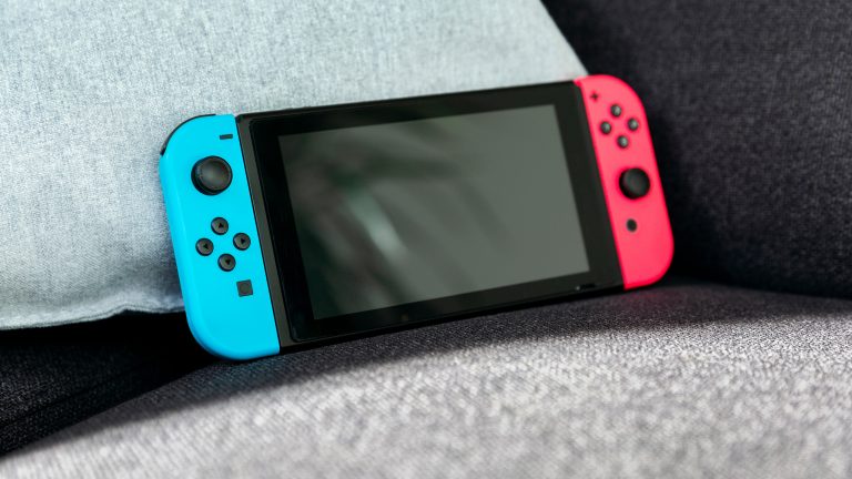 Nintendo Switch Online, Tarife, Vorteile und mehr Eine Nintendo Switch mit blauen und roten JoyCons lehnt an einem Kissen auf einer Couch.