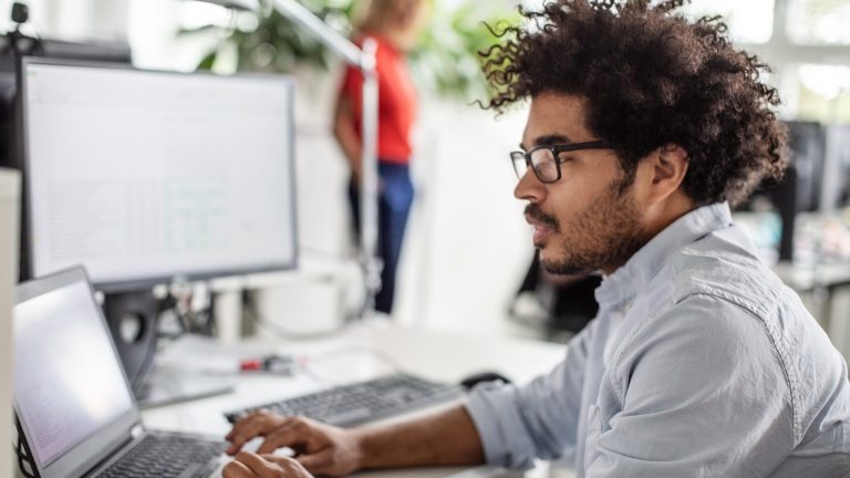 PDFs zusammenfügen, So klappt es Eine Person sitzt in einem Büro vor einem Laptop und nutzt das Touchpad.