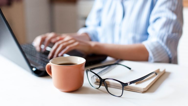 PDFs zusammenfügen, So klappt es Eine Person sitzt vor einem Laptop. Im Vordergrund sind eine Brille und eine Tasse Kaffee zu sehen.