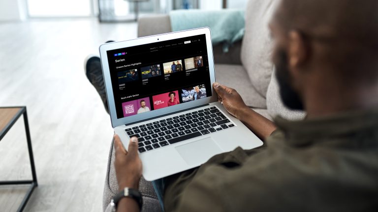 Eine Person sitzt auf einem Sofa und schaut auf ihrem Laptop in die RTL+-App.