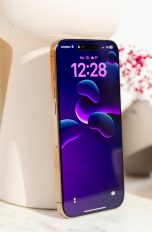 Ein iPhone 16 Pro Max in Wüstensand steht an eine Vase gelehnt auf einem Regal.