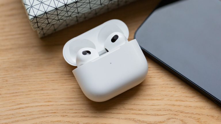 AirPods reinigen, Kopfhörerpflege leicht gemacht Ein offenes Ladecase mit zwei AirPods darin, daneben liegt ein iPhone auf einem Holzuntergrund.