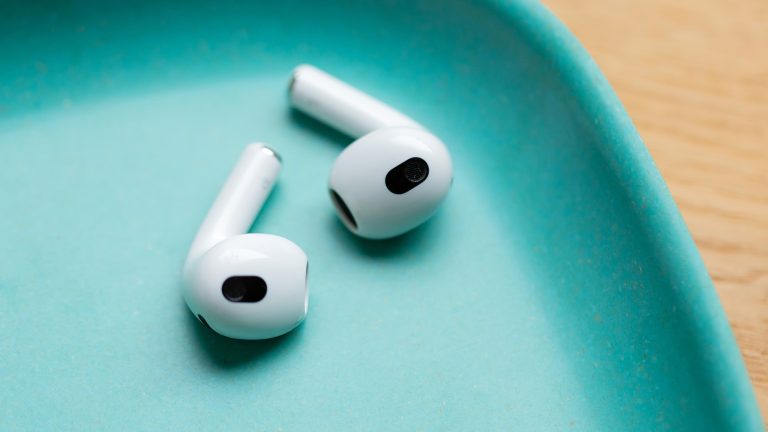 Zwei AirPods liegen in einer türkisfarbenen Schale auf einem Holzuntergrund.