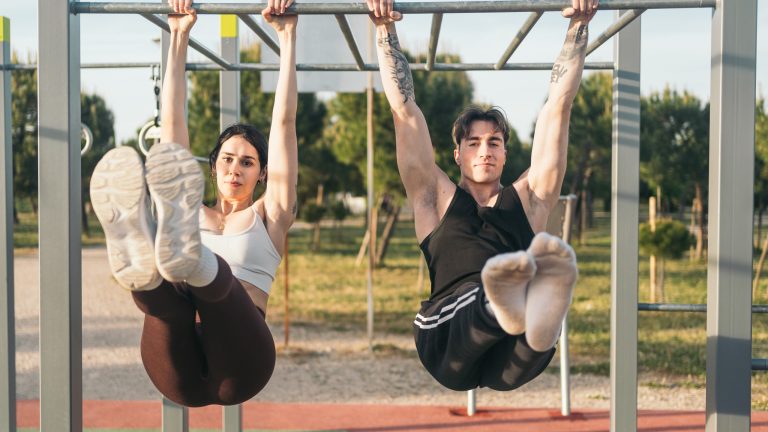 Calisthenics, Diese Apps unterstützen dich beim ultimativen Ganzkörpertraining Zwei Personen führen an einer Calisthenics-Station Hanging Leg Raises aus.