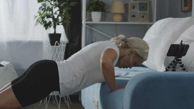 Calisthenics, Diese Apps unterstützen dich beim ultimativen Ganzkörpertraining Eine Person macht Push-Ups. Das Sofa dient dabei als Stütze. Das Smartphone steht auf einem Ständer auf der Couch.