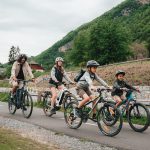 Eine Gruppe Radfahrender ist mit ihren Trekkingrädern auf einer Straße unterwegs. Im Hintergrund ist ein Berg zu sehen.