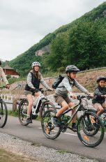 Eine Gruppe Radfahrender ist mit ihren Trekkingrädern auf einer Straße unterwegs. Im Hintergrund ist ein Berg zu sehen.