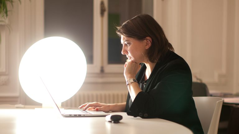 Praktische Gadgets fürs Homeoffice Eine Person sitzt vor einem Laptop. Neben ihr steht eine leuchtende Tageslichtlampe.